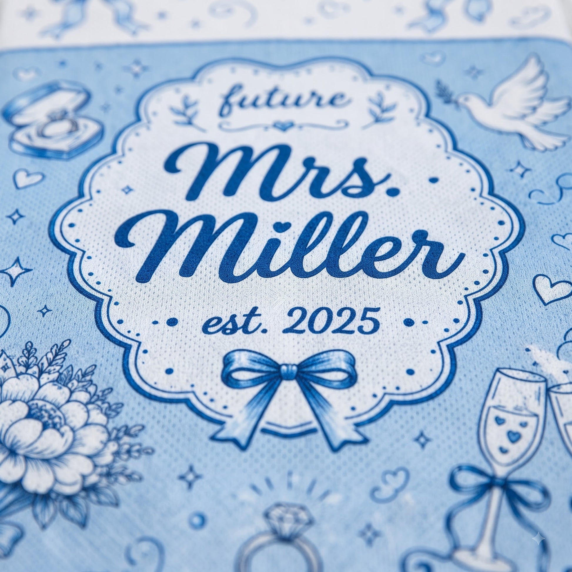A close-up of a light blue fabric item printed with a decorative white and navy label reading 'future Mrs. Miller est.