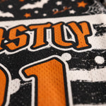 Close-up of a black, white, and orange athletic jersey fabric with a distressed graphic design, showing part of the lettering and number 31.