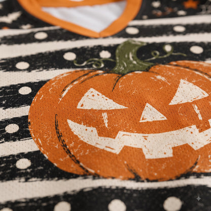 Close-up of a Halloween-themed garment featuring a large orange jack-o'-lantern with a distressed white face, set against a black and white polka-dot patterned background.