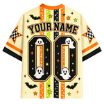 A Halloween-themed short-sleeve jersey-style shirt shown flat against a white background. The shirt has a cream base with orange, black, green, and yellow graphic accents, including stars, stripes, bats, ghosts, checkered stars, and large customizable text reading 'YOUR NAME' above two large '00' blocks.