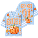 A short-sleeve t-shirt with a large autumn-themed pumpkin graphic on the back. The design features five pumpkins in various patterns (checkered, leopard print, polka dot, plaid) on a cream background, decorated with stars, leaves, and swirls in brown and gold tones.