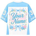 A customizable short-sleeve athletic jersey shown from the back, featuring a white center panel with a pink gingham background, large script text reading 'Your Name,' blue floral arrangements, bows, stars, and the number 3 on both sleeves.