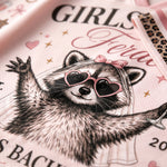 A close-up of a light pink printed fabric featuring a raccoon wearing heart-shaped sunglasses, a veil, and a pink bow, with partial text including 'GIRLS' and 'Bachelorette'.