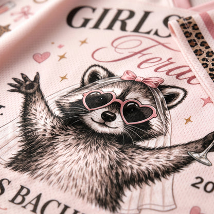 A close-up of a light pink printed fabric featuring a raccoon wearing heart-shaped sunglasses, a veil, and a pink bow, with partial text including 'GIRLS' and 'Bachelorette'.