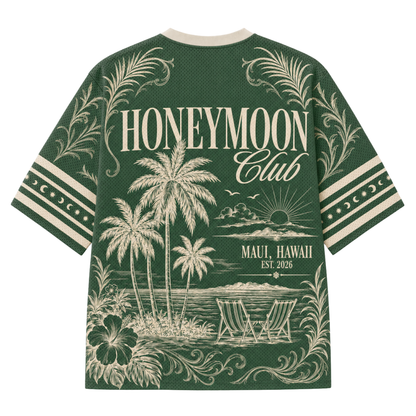A green short-sleeve t-shirt with a cream-colored graphic print on the back, featuring palm trees, beach chairs, and the text 'HONEYMOON Club' and 'MAUI, HAWAII EST. 2026'.