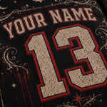 Close-up of a black jersey-style shirt with a distressed cream and red 'YOUR NAME 13' nameplate graphic and decorative scrollwork.
