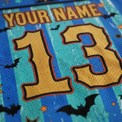 Close-up of a custom sports jersey featuring a Halloween theme. The back of the jersey has a teal and blue striped pattern with black bat silhouettes, small orange stars, and a gold embroidered number '13' outlined in black.