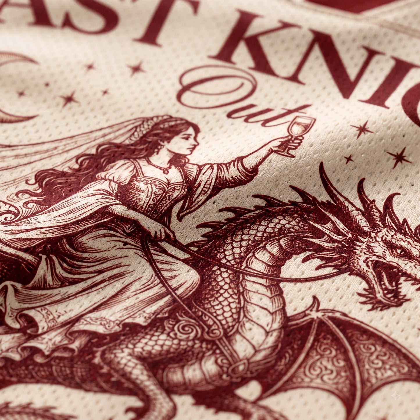 Close-up of a printed textile featuring a dark burgundy illustration of a knight in armor with a sword and a dragon, alongside partial text reading 'Knight Out' on a textured cream fabric background.