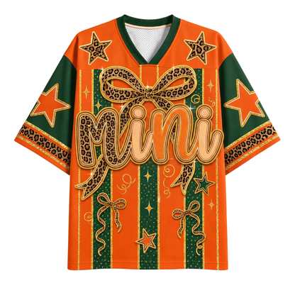 An orange and green short-sleeve V-neck t-shirt with a bold graphic design featuring leopard-print bows, stars, and the word 'Mini' in script across the front, shown on a plain white background.
