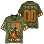 Back view of a customizable black short-sleeve jersey with orange and beige autumn-themed leaf patterns, a striped collar and cuffs, and 'YOUR NAME 10' printed in a distressed camouflage-style font.