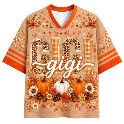 A black mesh short-sleeve jersey shown from the back, featuring customizable orange and pink text reading 'YOUR NAME' above large '00' numbers. The shirt is decorated with autumn-themed graphics including pumpkins, bows, leaves, stars, a witch hat, and a cauldron, with orange, pink, and black striped sleeve cuffs.