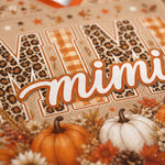 A close-up of a decorative autumn-themed graphic with the word "mimi" in white script outlined in orange, layered over large letters filled with leopard print and gingham patterns. Pumpkins, flowers, and fall foliage decorate the bottom, on a warm beige background.