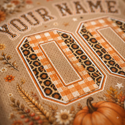 Close-up of a personalized sports jersey design with the number 00 in orange and brown leopard print and gingham, on a tan mesh fabric with autumn floral and pumpkin illustrations.