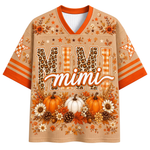 A short-sleeve V-neck t-shirt with a beige mesh-like texture, featuring an autumn-themed design. The shirt has orange trim on the collar and sleeves, 'MIMI' printed in large leopard-print and plaid letters, 'mimi' in script across the center, and pumpkins, flowers, and pinecones at the bottom.