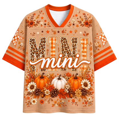A black mesh V-neck jersey shown from the front and back, decorated with a colorful Halloween theme. The front features a central graphic of a creepy doll character in a knit hat and scarf holding a drink and a cookie, surrounded by pumpkins, bows, and stars.