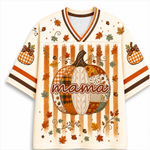 A short-sleeve V-neck jersey-style shirt with an autumn theme, featuring a large patchwork pumpkin graphic and the word 'mama' across the front, with orange, brown, and cream patterns.