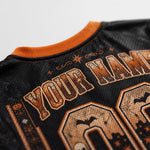 Close-up of a black mesh sports jersey with orange trim and distressed orange graphic text reading 'YOUR NAME' plus Halloween-themed decorative details.