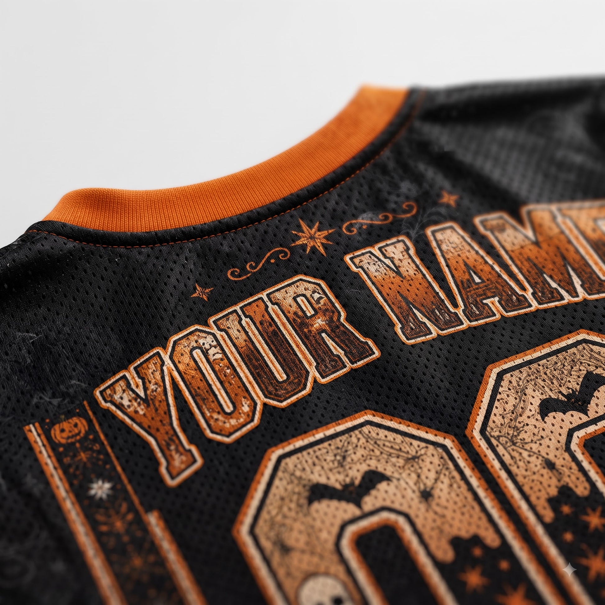 Close-up of a black mesh sports jersey with orange trim and distressed orange graphic text reading 'YOUR NAME' plus Halloween-themed decorative details.