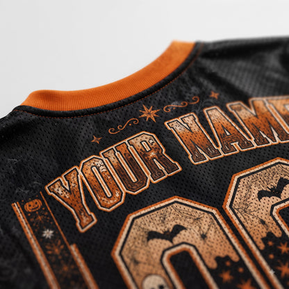 Close-up of a black mesh sports jersey with orange trim and distressed orange graphic text reading 'YOUR NAME' plus Halloween-themed decorative details.