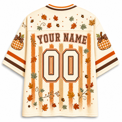 A cream-colored mesh football-style jersey shown from the back, featuring personalized print graphics including 'YOUR NAME', the number '00', orange and brown stripes, fall leaves, acorns, pumpkins, and decorative swirls.