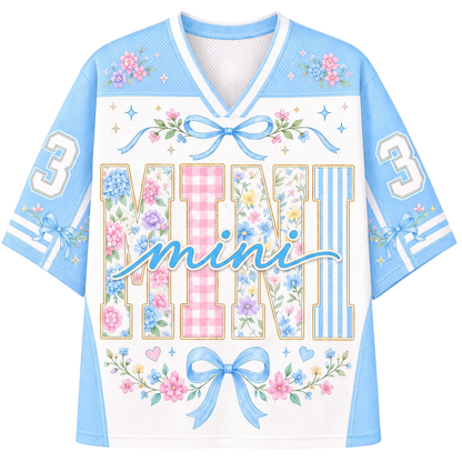 A custom football-style jersey shown from the front and back, featuring a brown and beige color scheme with a cartoon ghost holding a pumpkin and cup, surrounded by flowers and butterflies. The back has a placeholder text 'Your Name' and the front has 'Growing a little boo'.