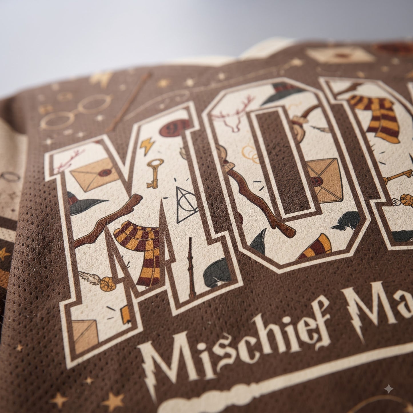Close-up of a brown knit garment featuring large decorative letters filled with whimsical illustrations and the text 'Mischief Ma.
