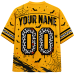 A yellow short-sleeve t-shirt shown from the back, featuring a Halloween-themed graphic design with 'YOUR NAME' and '00' in a black and white leopard print, decorated with black bats, spiderwebs, stars, and black paint splatters.