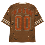 A brown short-sleeve t-shirt with a Halloween theme, featuring customizable text 'YOUR NAME' and '00' on the back in orange and white, decorated with orange jack-o'-lanterns, black bats, spiderwebs, and white stars.