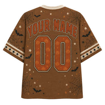 A brown short-sleeve t-shirt with a Halloween theme, featuring customizable text 'YOUR NAME' and '00' on the back in orange and white, decorated with orange jack-o'-lanterns, black bats, spiderwebs, and white stars.
