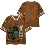 A brown short-sleeve V-neck t-shirt with a Halloween graphic print, shown in both front and back views. The front features 'MONSTER MASH' in orange text above a collage of classic horror characters including Frankenstein, Dracula, the Lurcher, a zombie, a ghost, a werewolf, and a jack-o'-lantern.