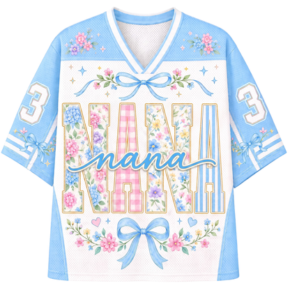 A light blue and white short-sleeve V-neck jersey-style shirt with floral and bow graphics. The front reads 'NANA' in large floral block letters with the word 'nana' in script across the chest, and the number 3 appears on both sleeves.