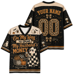 A Halloween-themed short-sleeve V-neck jersey shirt shown from both front and back. The design features a black and beige leopard-print base with orange text reading 'On My Way TO SPEND My Husband's MONEY,' ghost illustrations, a shopping cart graphic, and customizable text 'YOUR NAME' and number '00' on the back.