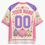 Customizable short-sleeve raglan-style jersey shown from the back, with cream body, purple shoulders and number panels, pink trim, floral and pumpkin motifs, and placeholder text 'YOUR NAME' and '00'.