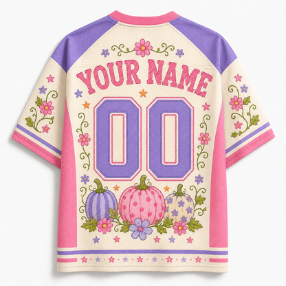 Customizable short-sleeve raglan-style jersey shown from the back, with cream body, purple shoulders and number panels, pink trim, floral and pumpkin motifs, and placeholder text 'YOUR NAME' and '00'.