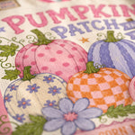 A close-up of a decorative autumn-themed printed surface with illustrated pumpkins, flowers, leaves, and the words “Pumpkin Patch” in pink and purple lettering.