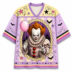 A short-sleeve V-neck t-shirt with a horror clown graphic on the front. The shirt features a light purple and pale yellow color-blocked design with black bat silhouettes, stars, and swirls, and a large central illustration of a creepy clown holding a pink balloon.