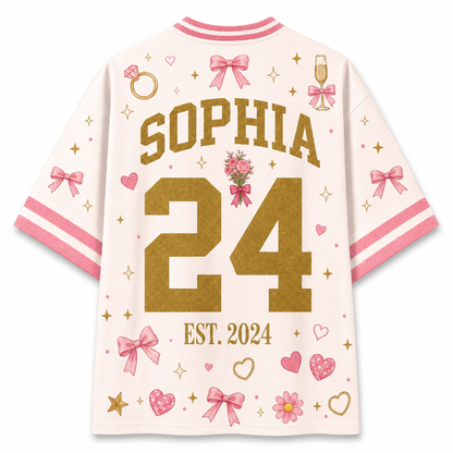 A white short-sleeve t-shirt with pink and gold custom graphics, featuring the name 'SOPHIA' and number '24' on the back, decorated with pink bows, hearts, stars, and a ring illustration.