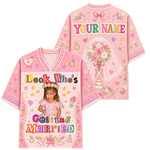 A pink short-sleeve V-neck t-shirt shown from both front and back, featuring customizable text 'Look Who's Getting Married' and 'YOUR NAME' with a bride illustration, hearts, flowers, and a small photo of a young girl.