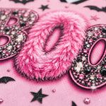 A close-up of a pink textured surface featuring a large fluffy pink letter 'O' in the center, flanked by glittery pink letters with rhinestones, black bat silhouettes, and black stars.