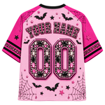 A pink short-sleeve jersey shown from the back, featuring black and pink rhinestone-style embellishments, customizable 'YOUR NAME' text, and large '00' lettering. The design includes black bats, spiderwebs, stars, and small pink gem accents on a light pink background.