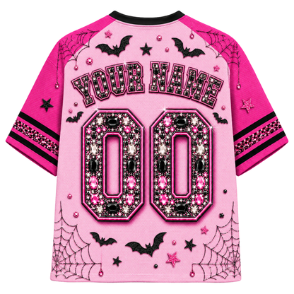 A pink short-sleeve jersey shown from the back, featuring black and pink rhinestone-style embellishments, customizable 'YOUR NAME' text, and large '00' lettering. The design includes black bats, spiderwebs, stars, and small pink gem accents on a light pink background.