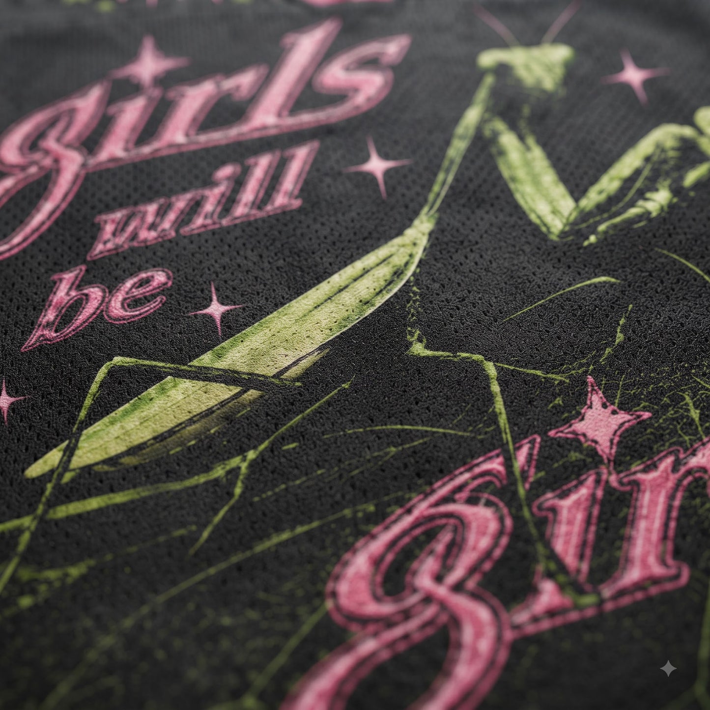 Close-up of a black mesh fabric featuring a green praying mantis graphic and pink gothic-style text reading 'girls will be'.