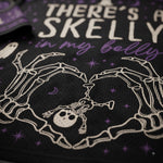 Close-up of a black mesh garment featuring a white skeleton graphic forming a heart shape around a small skull, with purple stars and the text 'THERE'S A SKELLY in my belly' in white and purple lettering.