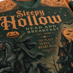 Close-up of a Halloween-themed graphic sweatshirt featuring the text 'Sleepy Hollow Dead and Breakfast' with a spooky illustration of a horse, pumpkin, moon, and haunted house.