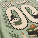 Close-up of a personalized Halloween-themed sports jersey fabric with a mint green mesh texture. The design features a large number '00' with cute cartoon ghosts inside, one wearing a witch hat and reading a book, and another ghost reading a book on the right.