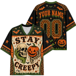 Front and back views of a Halloween-themed V-neck t-shirt. The shirt features a spooky graphic design with a skull, a skeleton hand holding a jack-o'-lantern, bats, pumpkins, leopard print patterns, and customizable text reading 'YOUR NAME' and 'STAY CREEPY'.