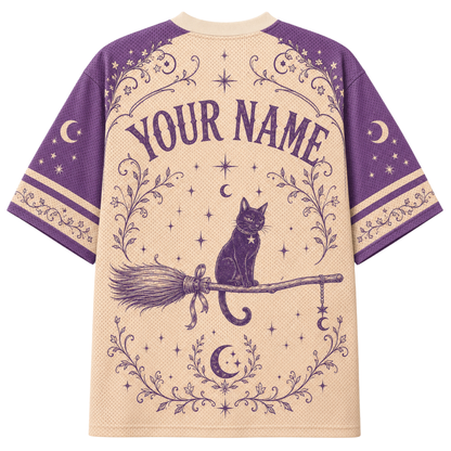 A short-sleeve t-shirt with a witch-themed graphic print. The shirt features a cream-colored body and purple sleeves, decorated with a purple illustration of a witch cat sitting on a broomstick, surrounded by stars, moons, and floral borders.