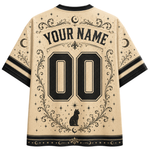 Back view of a beige short-sleeve jersey-style shirt with black celestial graphics, including moons, stars, ornate flourishes, a cat silhouette, and large customizable text reading 'YOUR NAME' and '00'.
