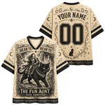Front and back views of a beige V-neck jersey-style shirt with black trim, featuring a vintage-style witch riding a black cat illustration on the front and customizable text 'YOUR NAME' and '00' on the back.