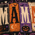 Close-up of a Halloween-themed fabric or print featuring large distressed block letters spelling part of a word, with black, orange, and purple panels, stars, bats, a crescent moon, spiderwebs, and a jack-o'-lantern.